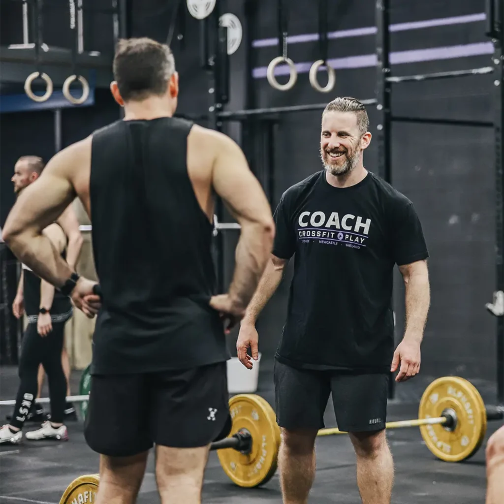 a photo of a coach wearing black t-shirt talking to one of the gym members