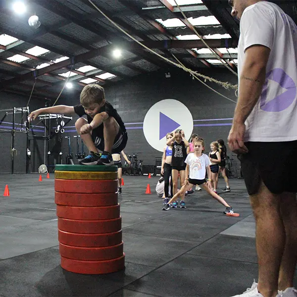 a kid on top of a stack of rainbow colored weights along with his coach Aaron