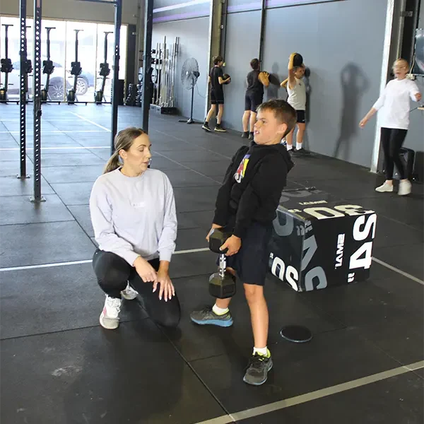a kid lifting a dumbell under a coach supervision