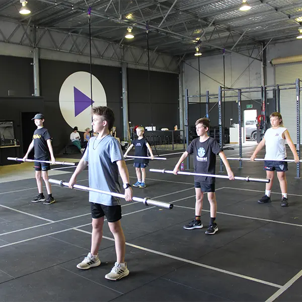 a group of kids holding a barbell handle with both their hands below waist